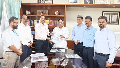 Senior officials and executives in a formal meeting exchanging documents in an office setting.