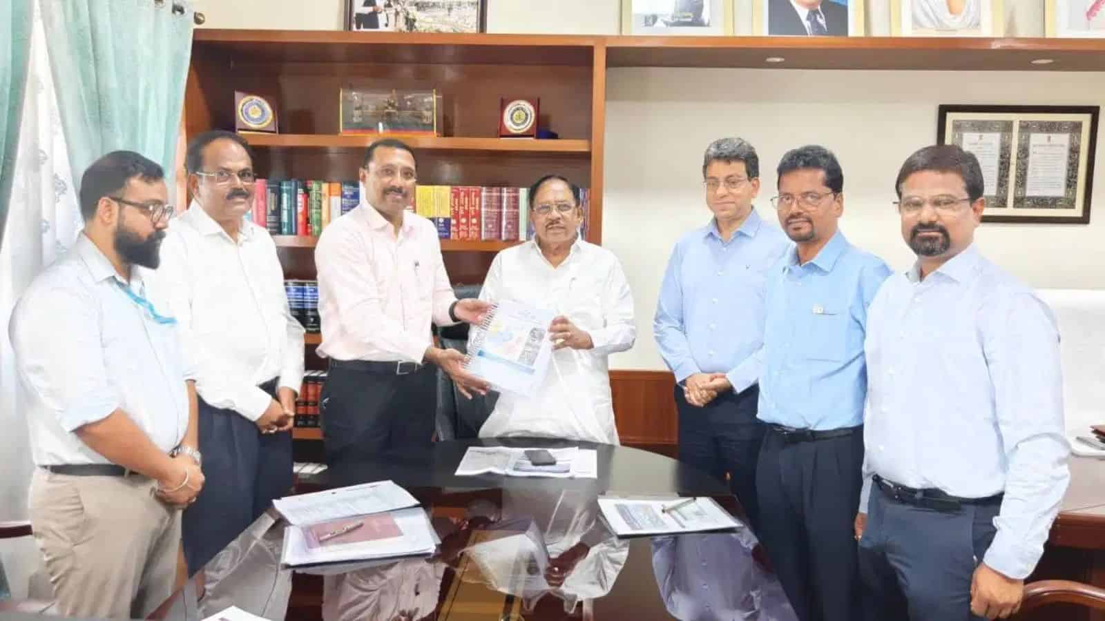 Senior officials and executives in a formal meeting exchanging documents in an office setting.