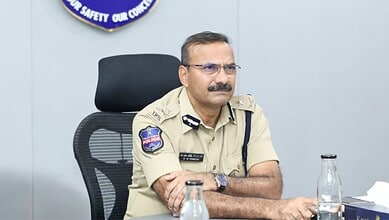 Police officer in uniform sitting at a desk during a meeting or press conference.