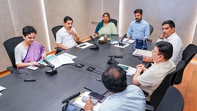 A woman and five men in a business meeting around a conference table with laptops and documents.