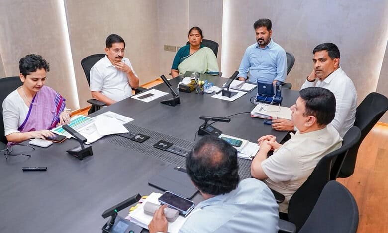 A woman and five men in a business meeting around a conference table with laptops and documents.