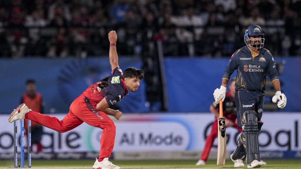 A cricket player in red diving to catch the ball near the stumps during a match.