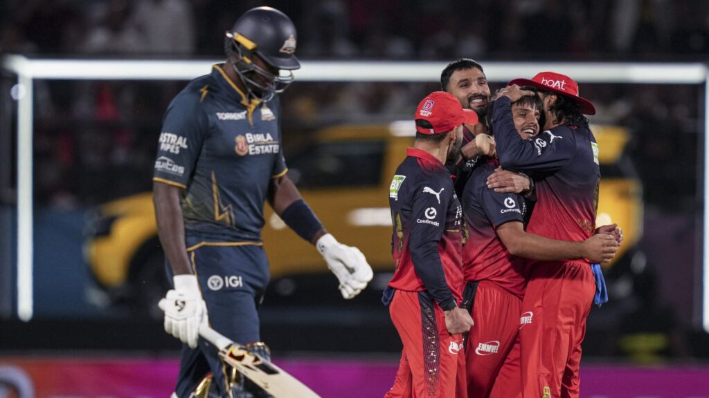 Celebrating cricket victory, team members embrace on the field, with a player in a blue uniform walking a.