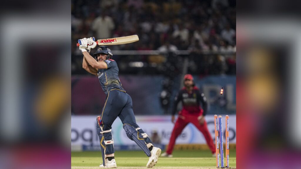 A woman cricketer batting during a match in a stadium with an umpire and players in the background.