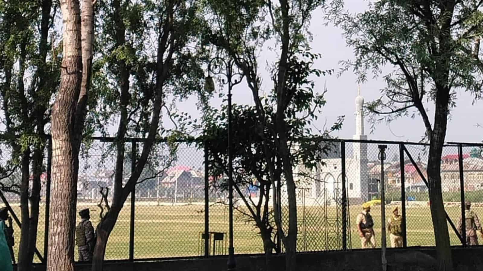 Bright outdoor sports field with players and trees, enclosed by a black fence, under a clear sky.