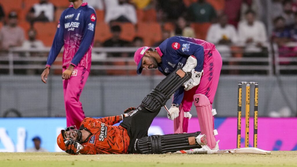 A cricket player helping a fallen teammate on the field during a match.