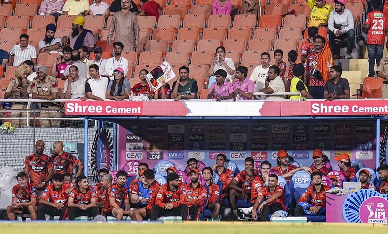 A football team sitting on the bench during a match at a stadium with spectators in the background.
