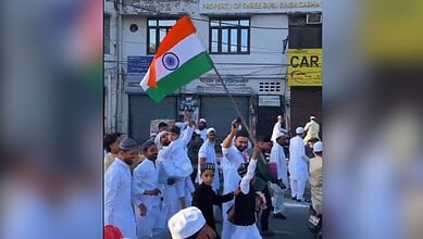 Indian flag being waved during a public demonstration in a busy street with people dressed in traditional.