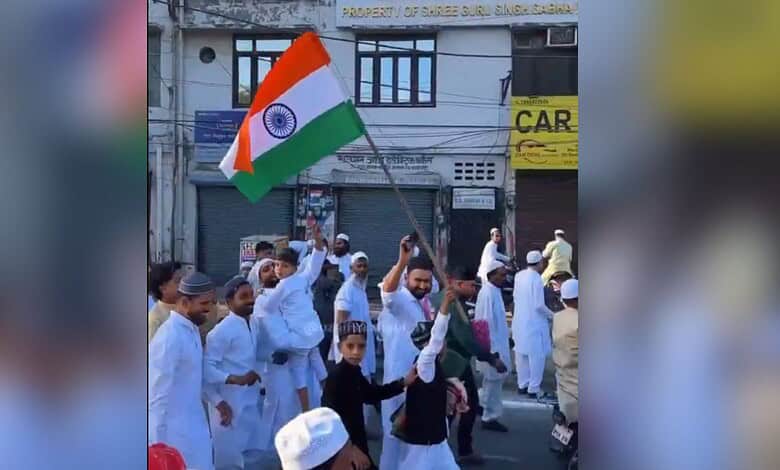Indian flag being waved during a public demonstration in a busy street with people dressed in traditional.