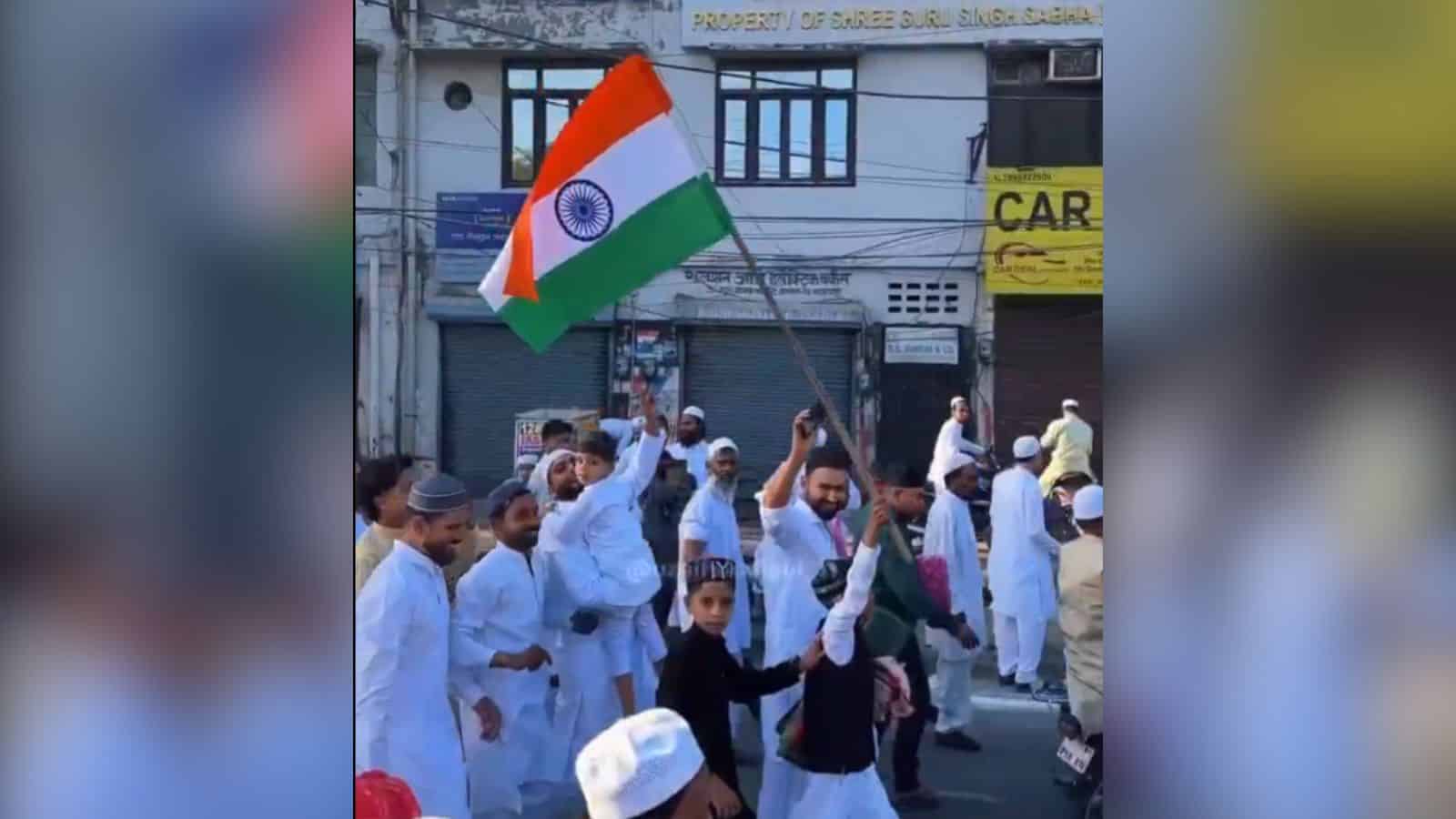 Indian flag being waved during a public demonstration in a busy street with people dressed in traditional.