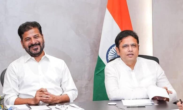 Two men in white shirts sitting at a desk with Indian flag in the background, smiling and engaged in disc.
