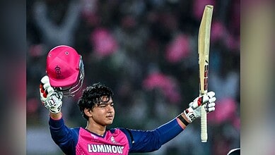 Cricketer celebrating with bat and helmet during a match, wearing a pink and blue uniform, in a stadium w.