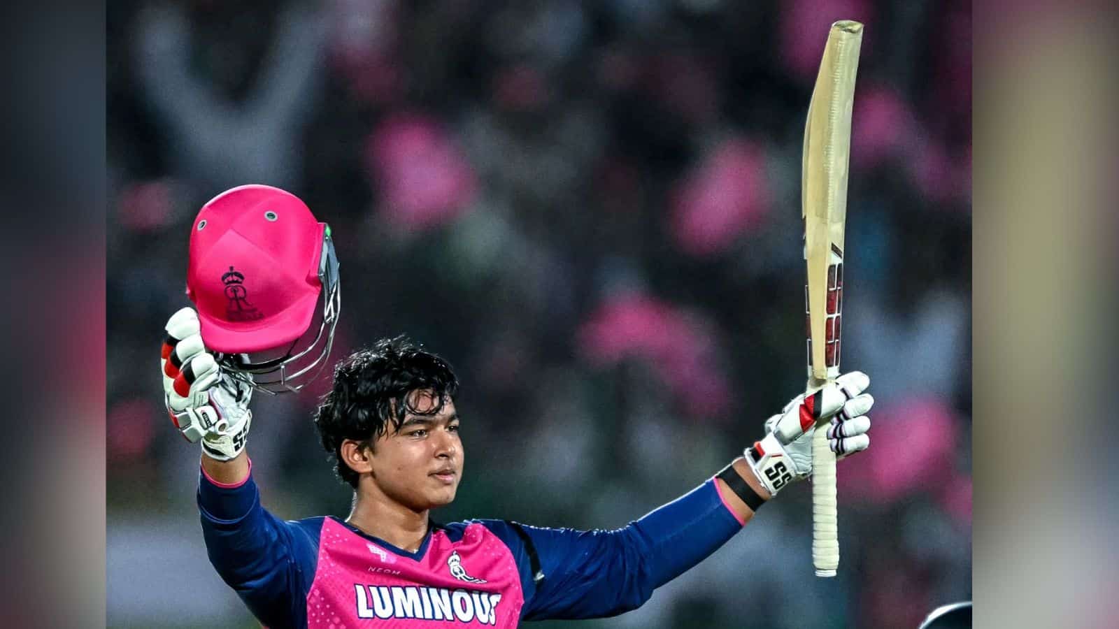 Cricketer celebrating with bat and helmet during a match, wearing a pink and blue uniform, in a stadium w.