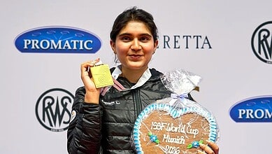 Young female athlete holding a gold medal at the ISF World Cup in Mumbai, standing in front of a promotio.