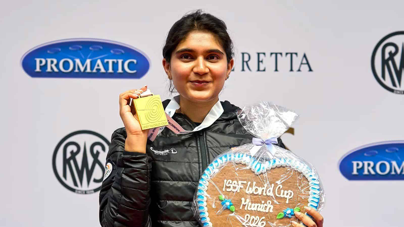 Young female athlete holding a gold medal at the ISF World Cup in Mumbai, standing in front of a promotio.