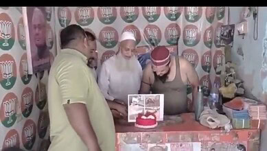 A man cutting a birthday cake with others gathered around in a room decorated with political party symbol.