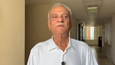A senior man with grey hair and a white shirt walking in a modern building corridor.