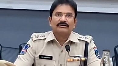 A police officer speaking at a press conference, wearing a beige uniform with badges and a microphone.
