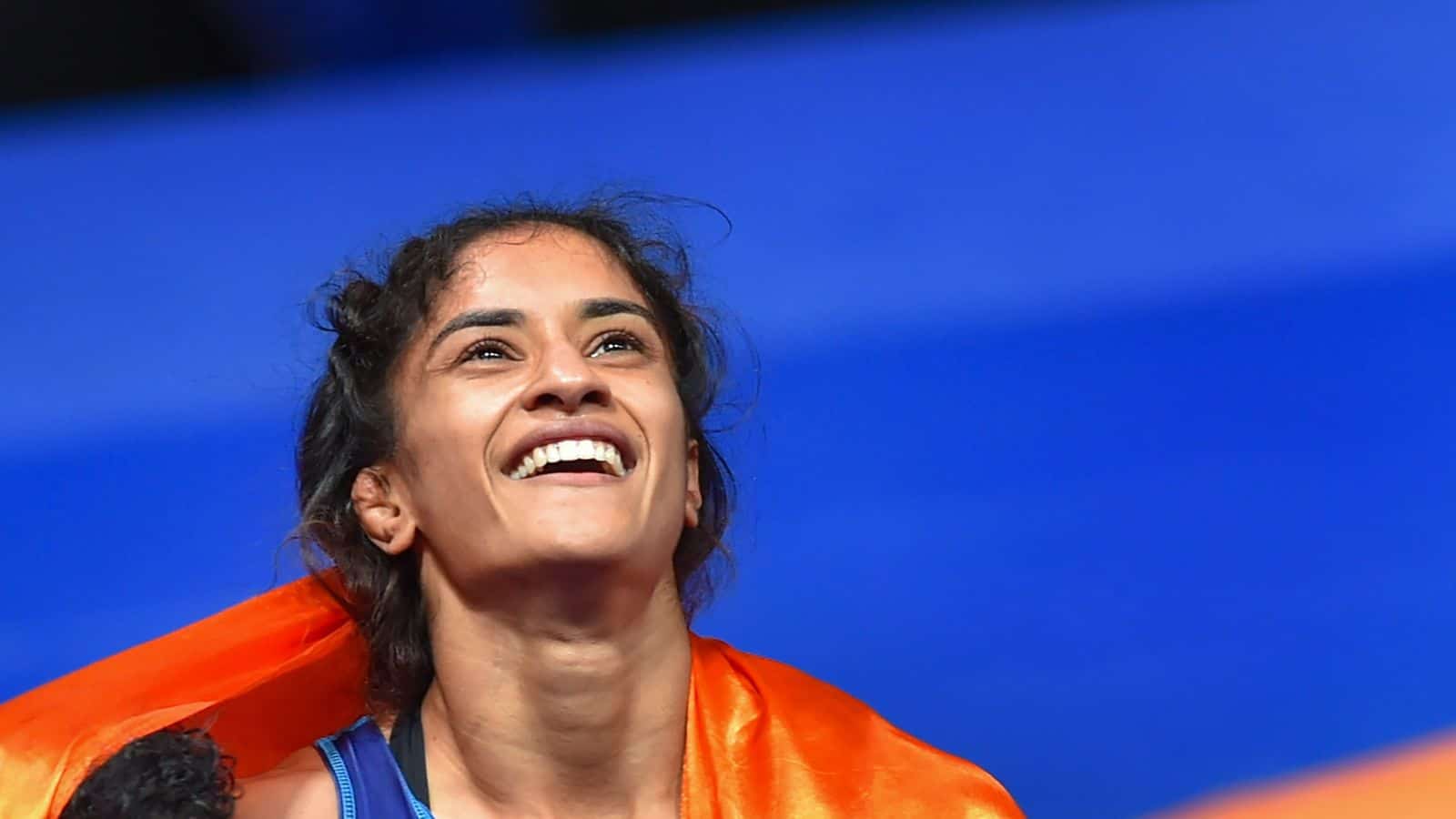 A woman smiling confidently with a vibrant orange scarf against a blue background, representing empowerme.