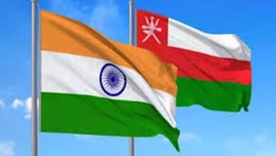 India and Oman national flags waving in the wind against a blue sky.