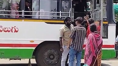 A man in a beige shirt talking to a group of women and men near a bus in an outdoor setting.