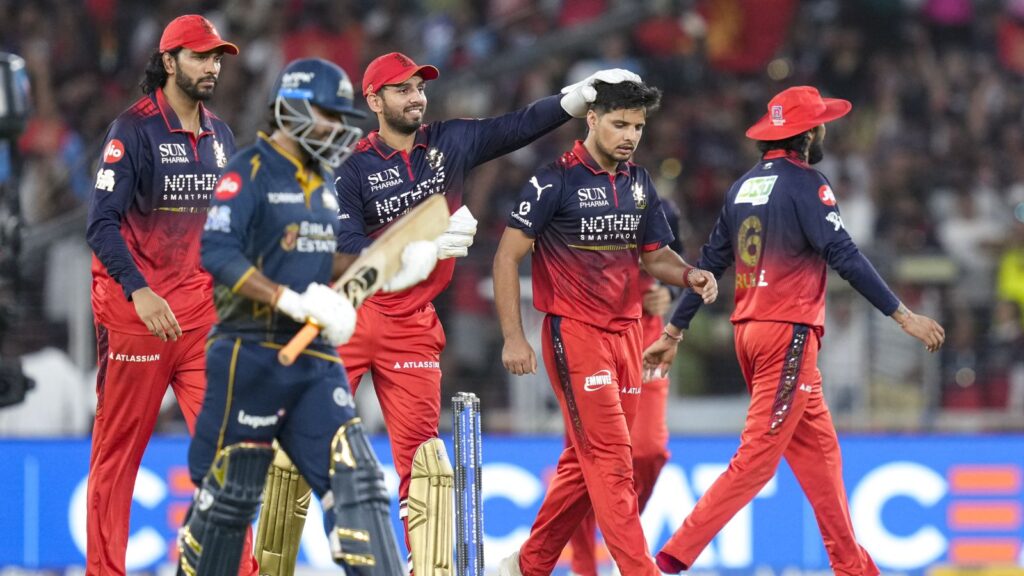 A cricket team celebrating on the field during a match, with players in red and blue uniforms.
