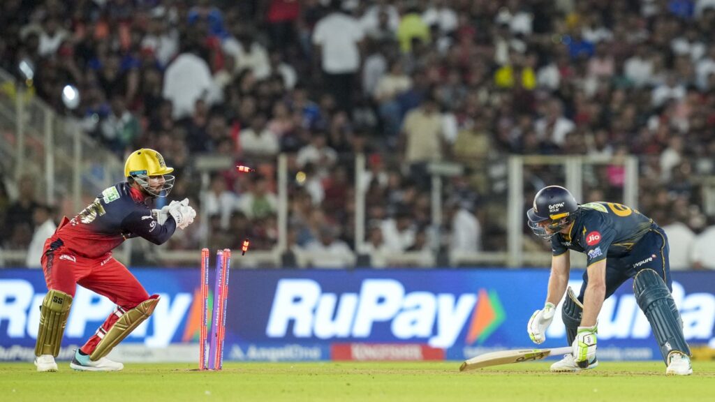 A cricket player in yellow helmet and red uniform fields the ball during a match at a packed stadium.