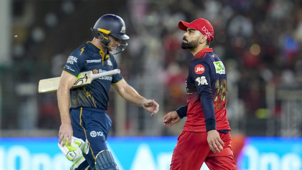 A cricket player in blue and yellow uniform shaking hands with a player in red and blue uniform on the fi.
