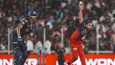 A young cricket player in red uniform bowling on the pitch during a match.