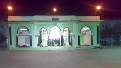 Bright green mosque entrance illuminated at night with arches and decorative elements, showcasing Islamic.