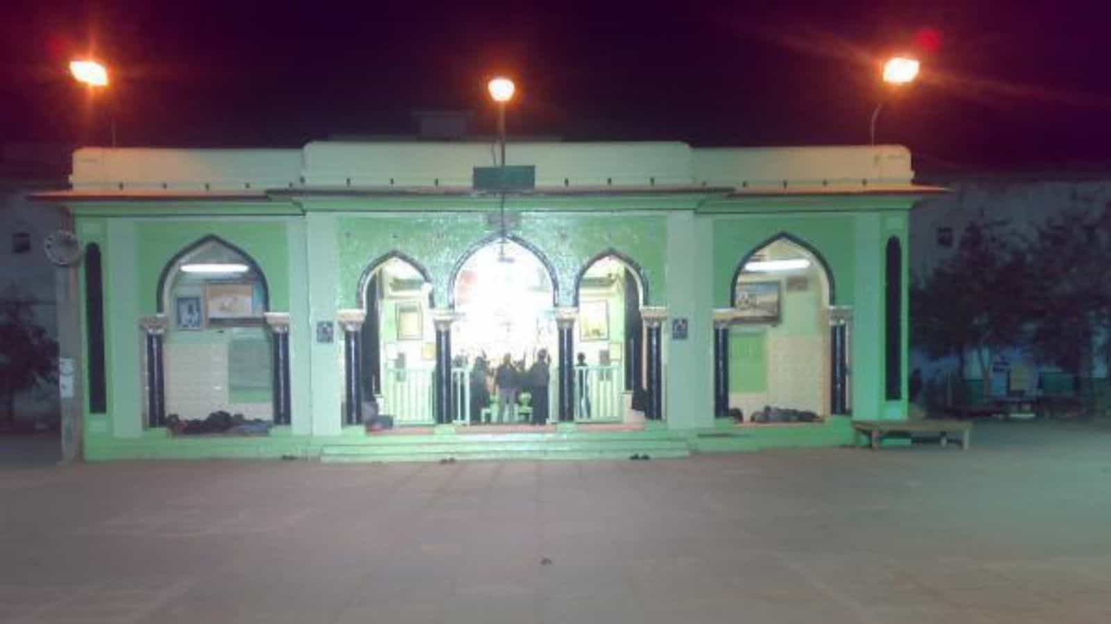 Bright green mosque entrance illuminated at night with arches and decorative elements, showcasing Islamic.
