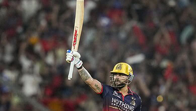 A cricket player celebrating with bat raised during match at a packed stadium.