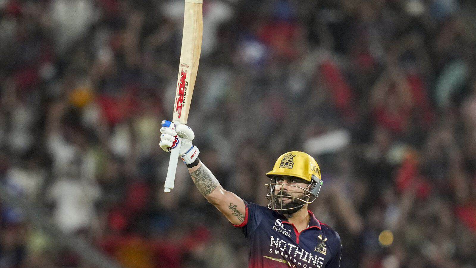 A cricket player celebrating with bat raised during match at a packed stadium.