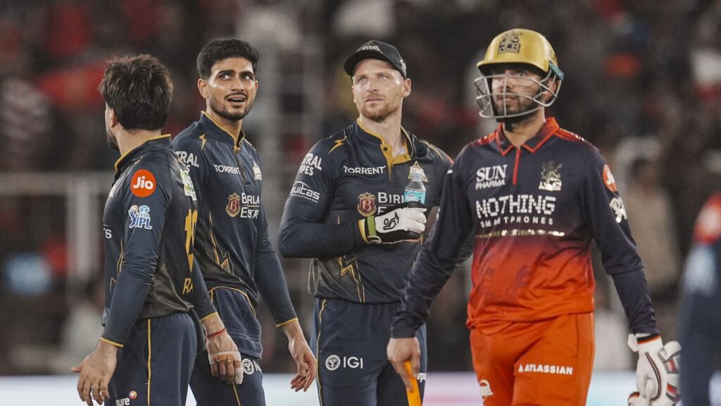 A cricket team celebrating on the field during a match, players in navy blue and orange uniforms.