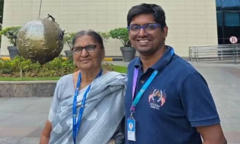 A young man and an elderly woman smiling outdoors at a corporate or conference event, both wearing lanyar.