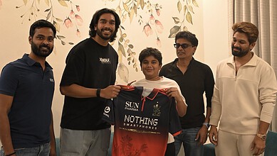 Group of five men, including a young boy, smiling and holding a smartphone and a jersey in an indoor sett.
