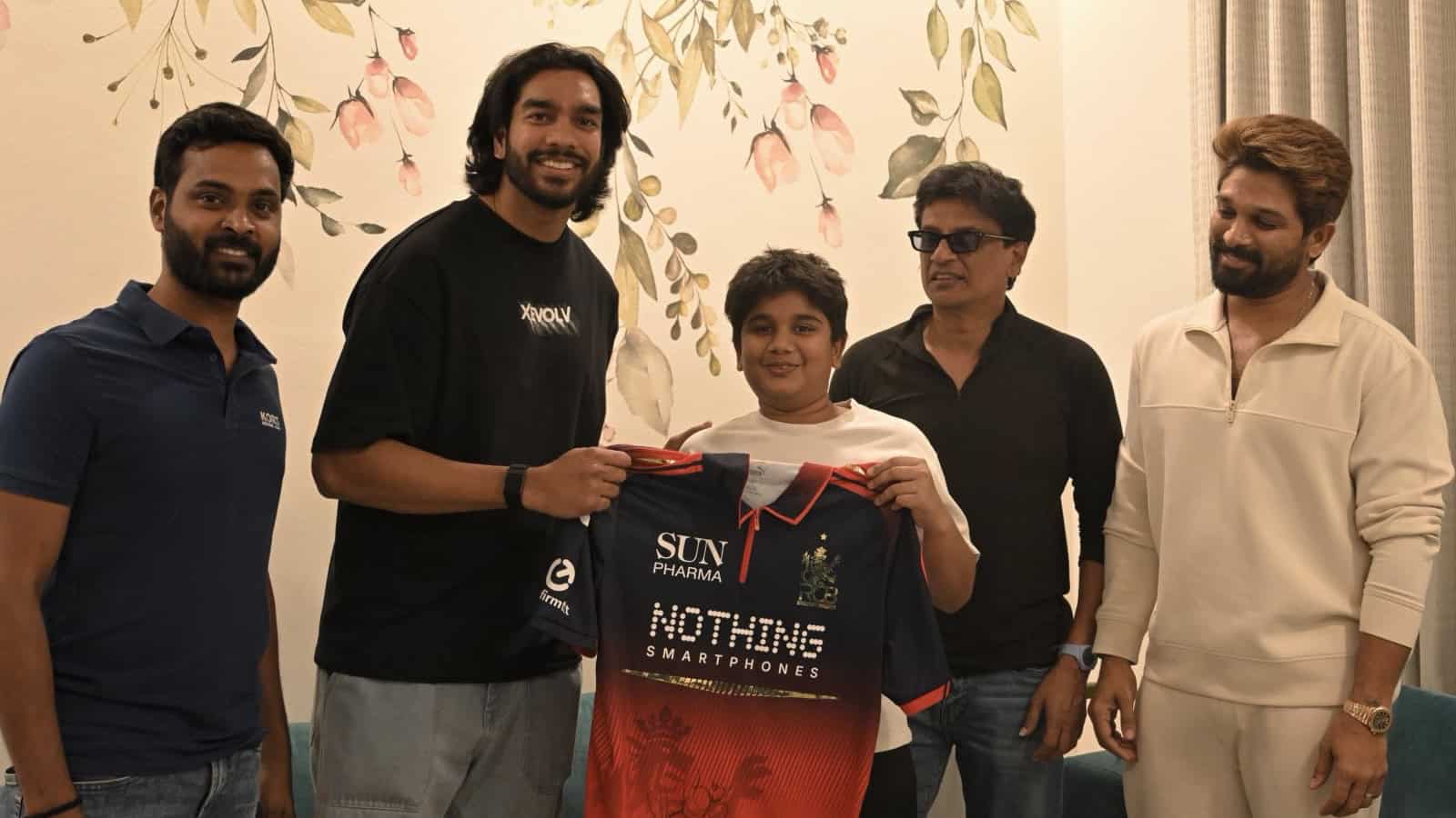 Group of five men, including a young boy, smiling and holding a smartphone and a jersey in an indoor sett.