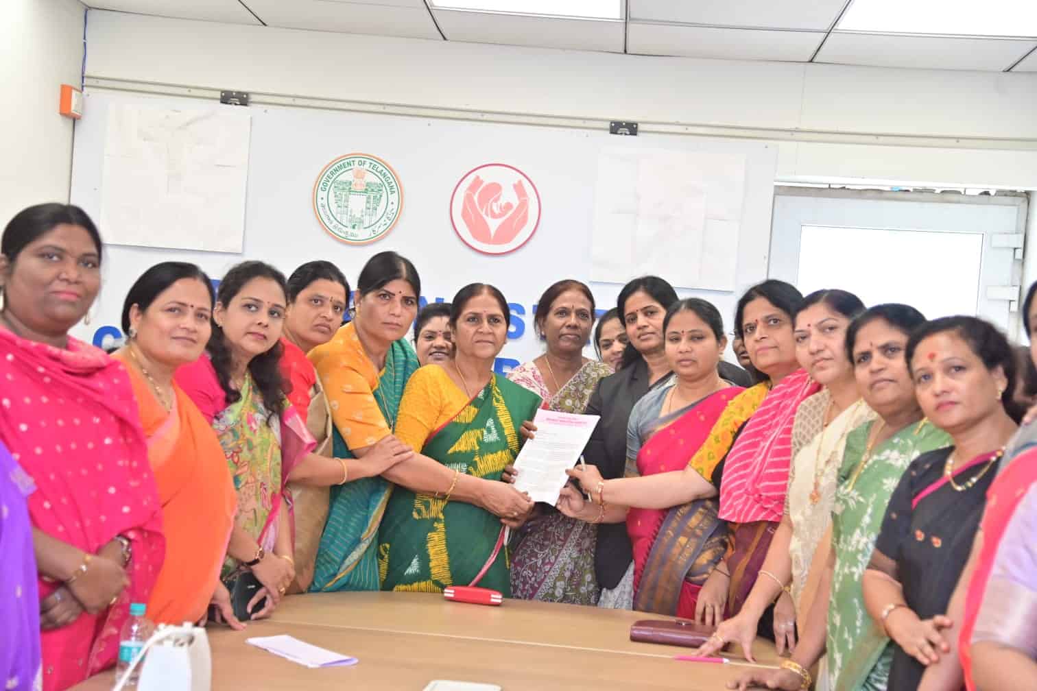 Women in colorful traditional attire participating in a formal meeting or award ceremony in an office set.