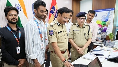 Police officers and civilians examining a laptop at a police station, with maps and flags in the backgrou.