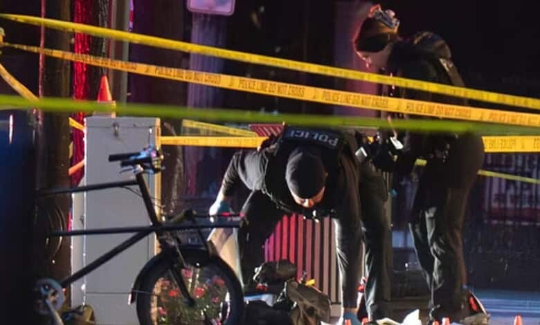 A man working on a bicycle at night, surrounded by police tape and officers, in an urban setting.