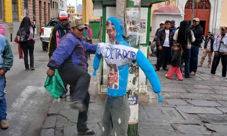 A woman with a blue headscarf and grey pants standing next to a utility pole in a busy urban street scene.