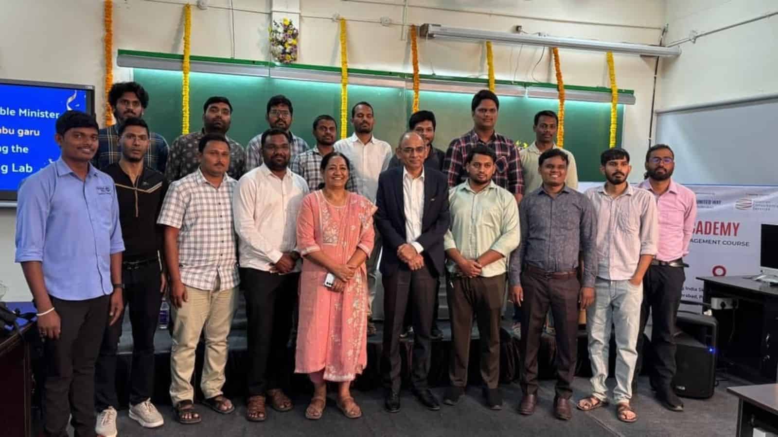 Group of university students and faculty members posing together at an academic event, with a green chalk.