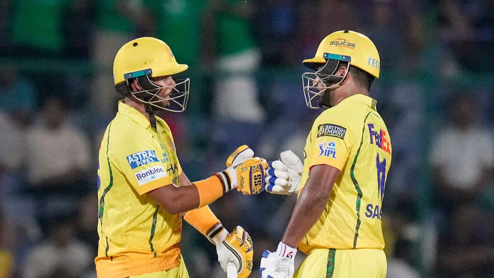 Two cricket players in yellow uniforms exchanging a fist bump during a match.