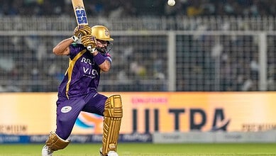 Cricketer in purple and gold uniform batting with a cricket bat during a match at a stadium.
