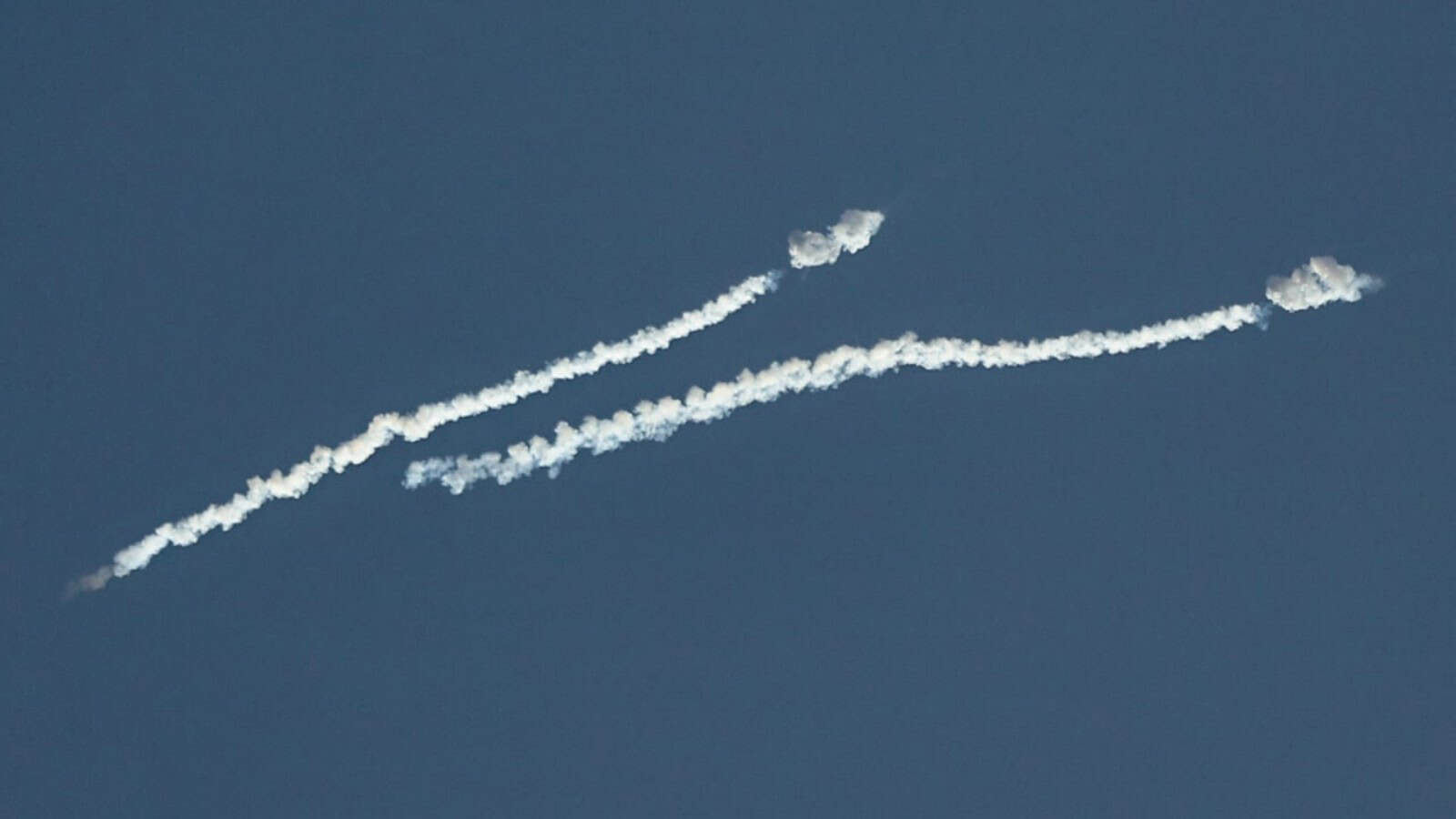 Image of missiles and drones flying in the sky amid Iran war tensions, with smoke trails visible.