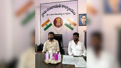 Indian political leaders seated at a desk with national flags and a banner in the background.
