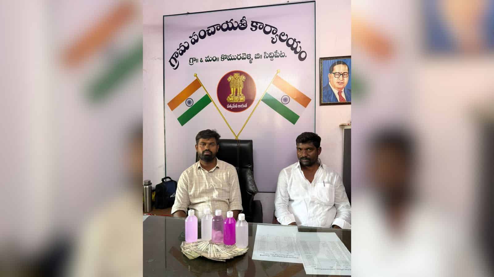 Indian political leaders seated at a desk with national flags and a banner in the background.