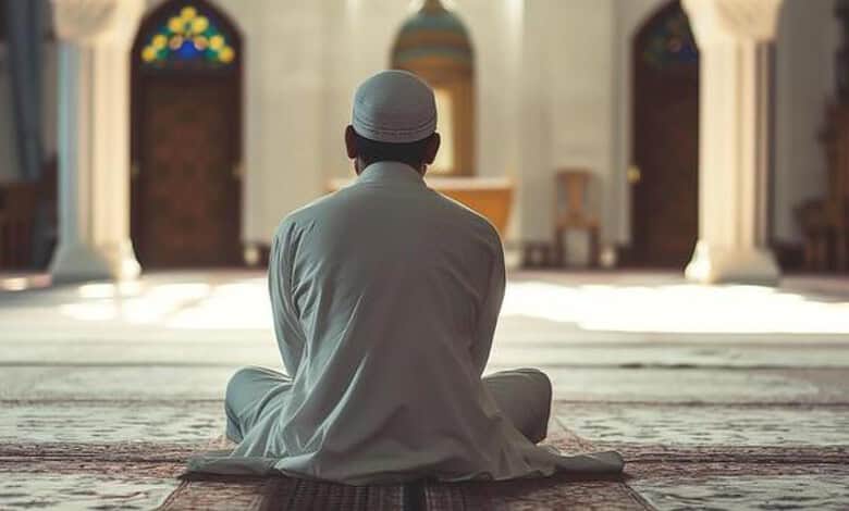 Serene Muslim man praying inside a mosque with intricate stained glass windows in the background.