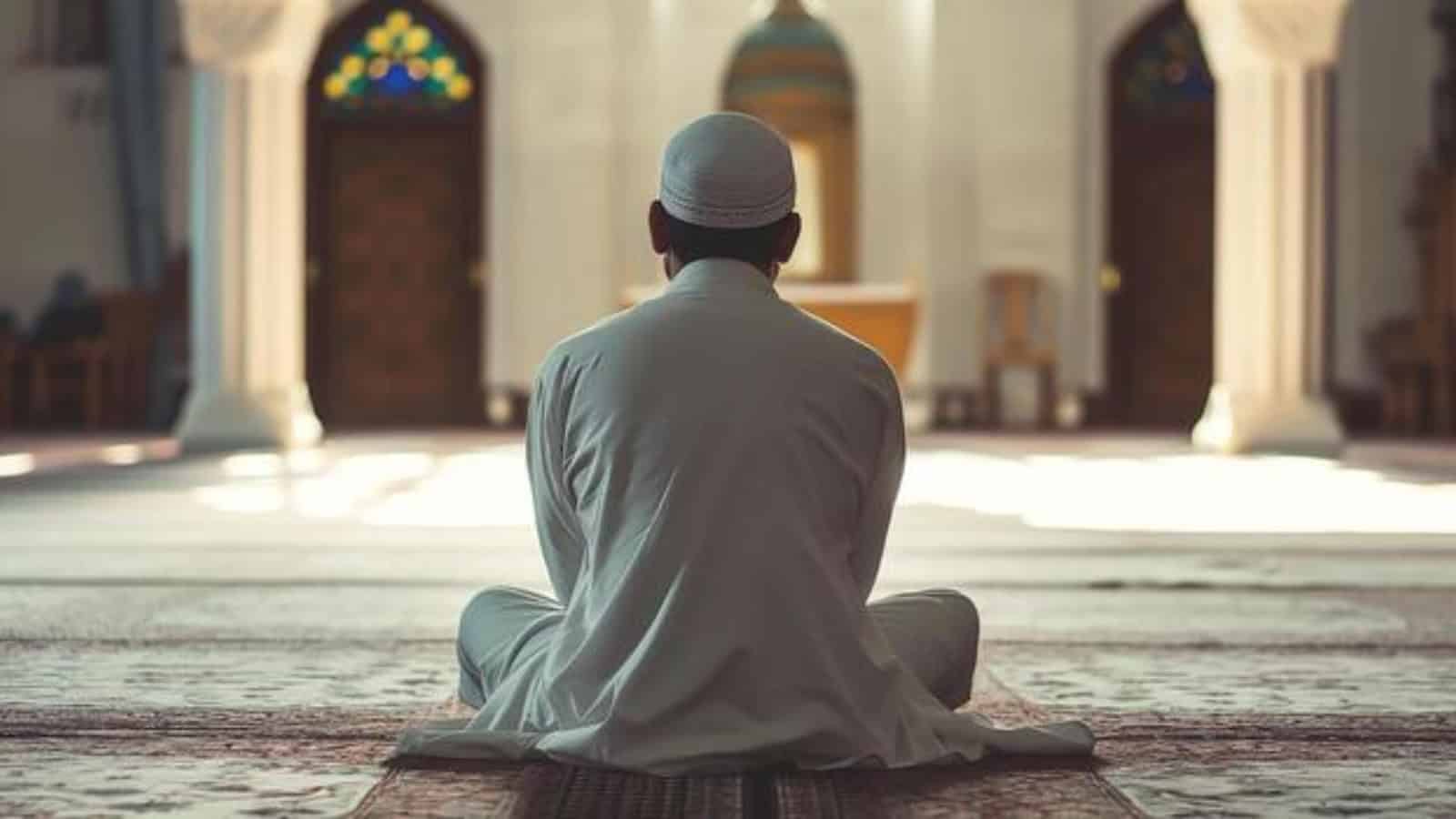 Serene Muslim man praying inside a mosque with intricate stained glass windows in the background.