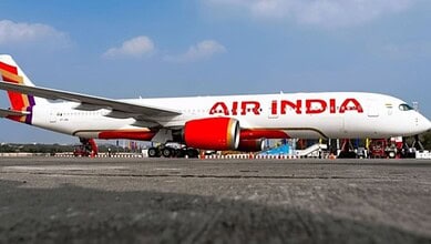 Air India commercial airplane parked on runway under blue sky with clouds.